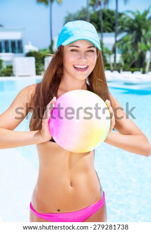Happy woman playing with ball in swimming pool on luxury beach resort, enjoying active water game, summer vacation concept
