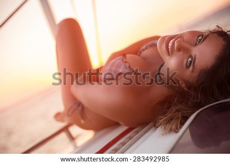 Beautiful woman lying down on the deck of sailboat and tanning, enjoying mild sunset light, summer adventure in the sea