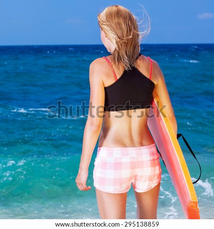 Sportive woman on the beach, slim girl standing back side and enjoying beautiful sea view with surfboard in hand, active summer vacation