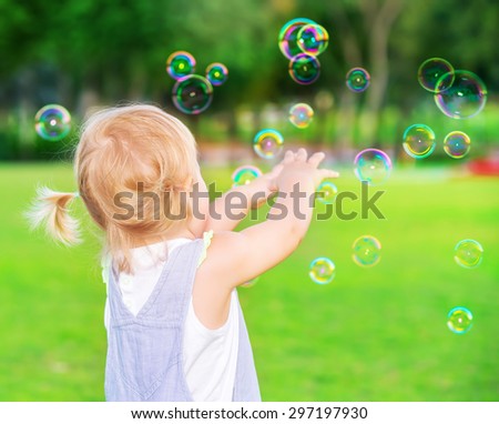 Little baby girl try to catch soap bubbles, having fun outdoors, playing games in the park, happy carefree childhood