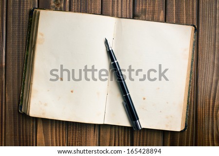 top view of old open book with fountain pen on wooden table