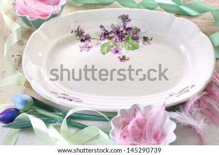 Plate with painted flowers on beige background with frame and woody tulip and bird feathers