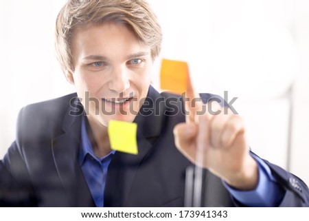 Businessman putting up notes .Young, handsome man of success in the office room glued yellow notes
