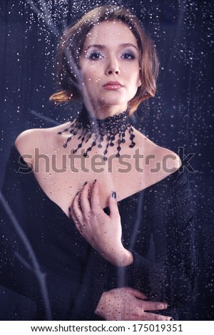 Glamour necklace-portrait of a woman in black . Beautiful mysterious woman dressed in black dress and lace necklace looks out the window the night