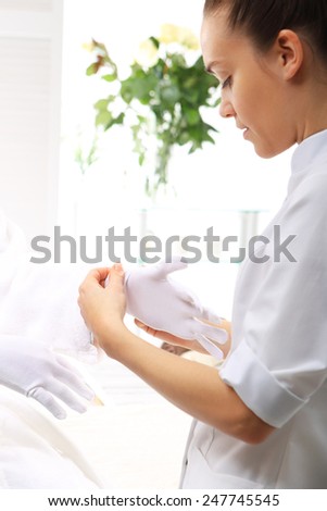 Paraffin hand treatment, beauty institute. Woman beautician applied to cotton gloves paraffin treatment