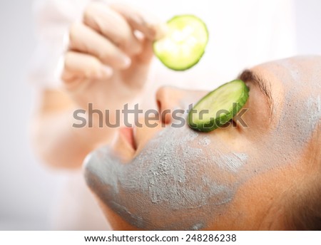 Green clay, cosmetic surgery, skin cleansing. Cosmetic procedure woman\'s face in the mask mitigating and cucumber slices on eyes