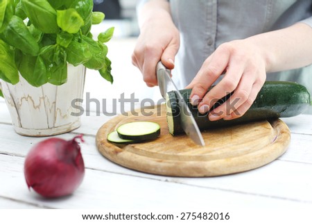 Zucchini, woman preparing a meal. Hands woman standing in the kitchen while chopping zucchini
