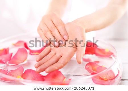 Reflexology, a gentle hand massage . Beauty ritual for hands. Care treatment of hands and nails woman hands over the bowl with rose petals