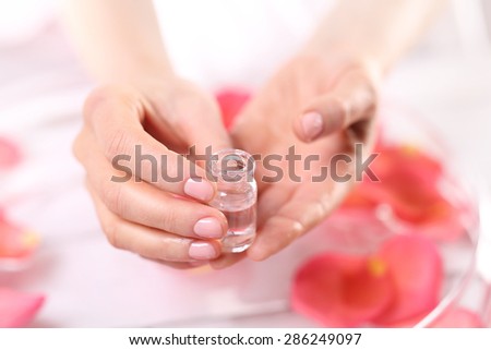 Manicure, skin whitening, cosmetic ampoule . Treatment hand and nail care, women hold hands vial of rose oil over the bowl with rose petals