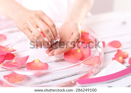 Aromatic bath hand. Treatment hand and nail care, women hold hands vial of rose oil over the bowl with rose petals