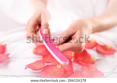 Manicure, nails woman saws. Woman saws nail file nails pink paper