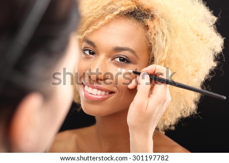 Make up. Well groomed facial skin. Dark skinned woman\'s face overlaid with cream under the eyes