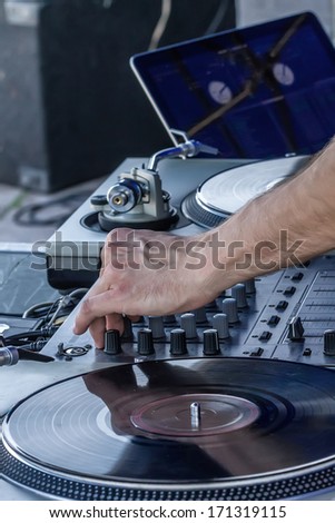 hand of DJ tweaking knobs and moving sliders on mixer,