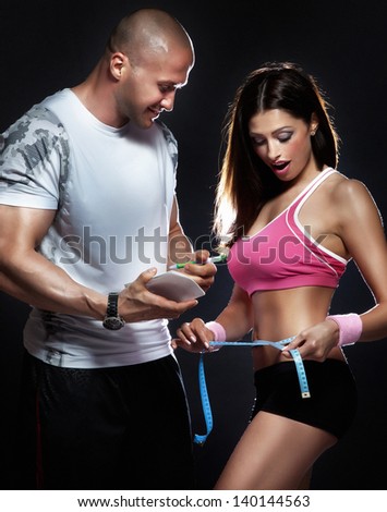 Conceptual photo of beautiful young brunette woman measuring her body with professional trainer.