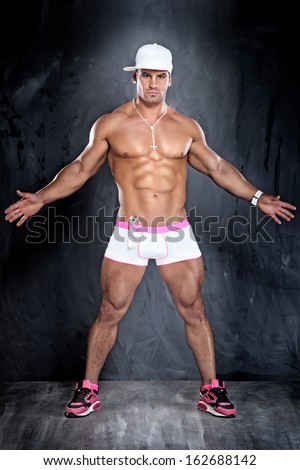 Muscular young handsome man posing in studio, wearing panties, looking at camera. Perfect body.