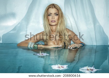 Portrait of beautiful blonde woman relaxing in blue water, looking at camera. Girl with long hair