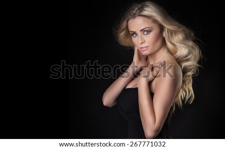 Delicate blonde young woman with long curly hair looking at camera over black background.