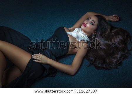 Elegant sexy brunette woman lying on the floor in black fashionable dress. Girl with ceremonial makeup.