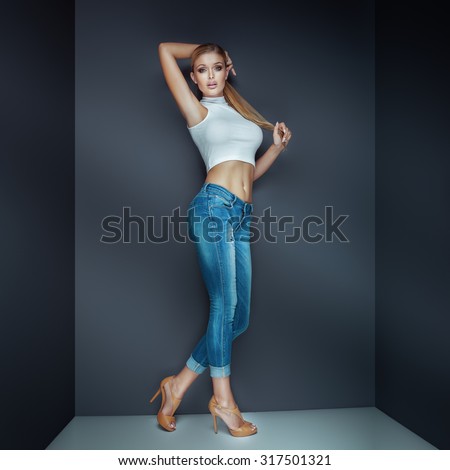 Sexy blonde woman posing in studio wearing fashionable jeans.