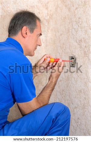 The electrician repairs electrical wall outlet