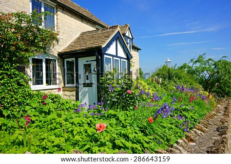 A beautiful quaint Cotswold country Cottage and garden in summer with blue sky and clouds, in the heart of The Cotswolds, Gloucestershire, United Kingdom