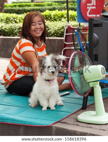 BANGKOK, THAILAND - MARCH 13, 2011: strong heat, probably, owing to global warming; young woman and her pet dog getting relief from the hot weather with a cooling fan in Bangkok on March 13, 2011.