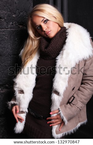 Beautiful blond woman in a fur near bricks wall