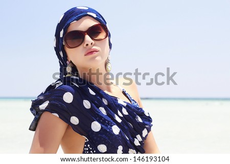 Beautiful woman in sunglasses on the beach. Arabian style. Blue scurf