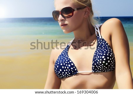 Beautiful Young Woman in Sunglasses on Beach.Flecks of Sunlight.Blue Sky. Summer Wear. Beauty Fashion Girl in Bikini. Nature Background