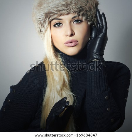 Beautiful Fashion Girl in Fur Hat. Beauty Blond Woman in Leather Gloves. Black sweater. Winter Fashion. Light Background