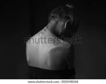 young woman with naked back over black background. sad girl