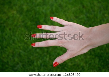 woman\'s hand with red varnish and green grass