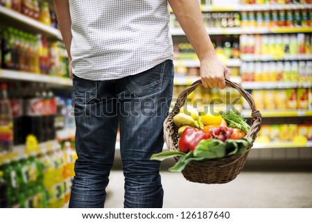 A person holding a basket of vegetables while walking in a grocery aisle