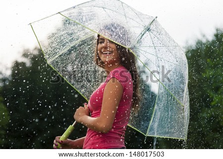 Young woman standing in summer rain with umbrella