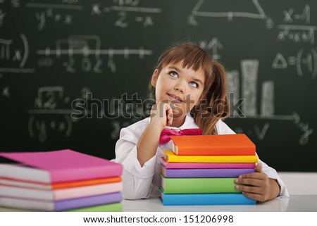 Cute little schoolgirl sitting in classroom with her books and dreaming