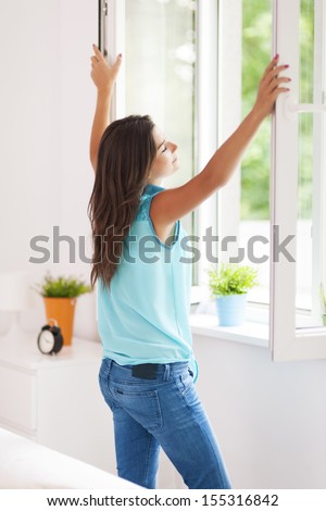 Young woman opening window in living room