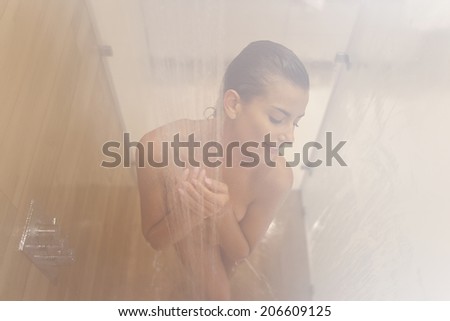 Beautiful woman relaxing under a hot shower, shooting through the steam