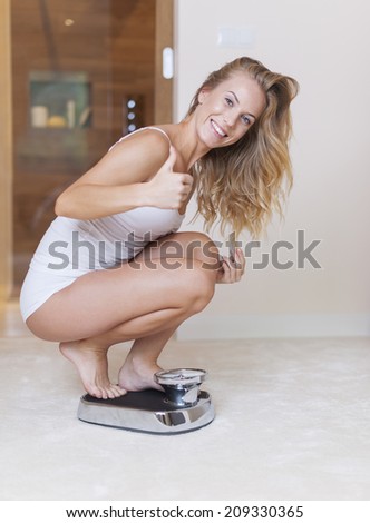 Happy woman on weighing scale showing thumb up