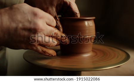 Unknown clay artist forming jar from wet clay piece in workshop. Unrecognized master modeling product in studio on potters wheel. Closeup man hands sculpting in pottery. Stockfoto © 