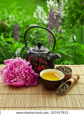 Teapot with bowl of jasmine green tea and peony flower