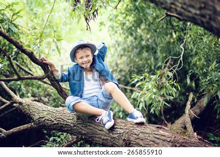 Boy sitting on a tree branch, dressed in a blue suit and hat, laughs , hand holds the hat
