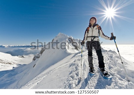 View from above: a woman looking over the horizon on a mountain peak, with sun on her back and a scenic view of the valley below hidden in the clouds in the background