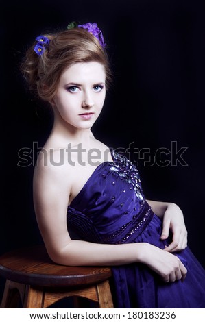 Elegant young blonde woman in a violet dress on the black background