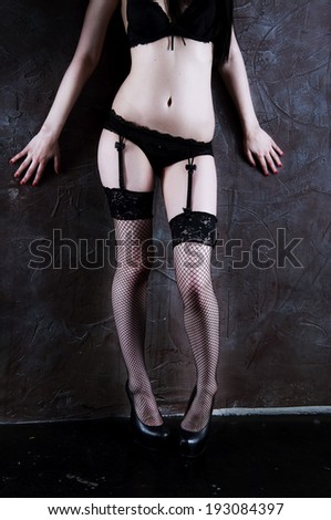 Woman in the black underwear standing at the wall wearing bra, panties, stockings and suspenders