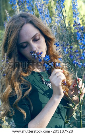 Sensual redheaded woman in sunset light smelling blue flowers