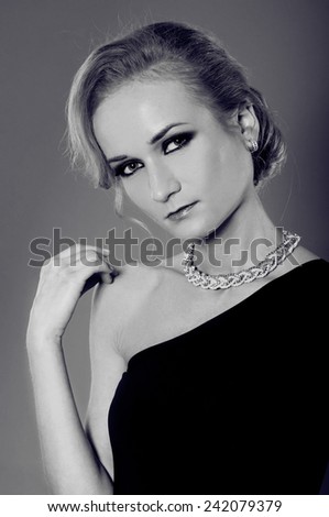 Black and white portrait of beautiful blonde woman in elegant black dress with diamond ring, earrings and necklace