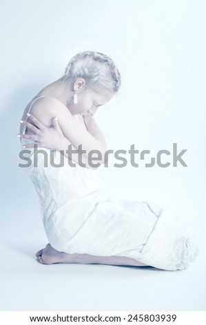 White woman sitting alone in white room hugging herself
