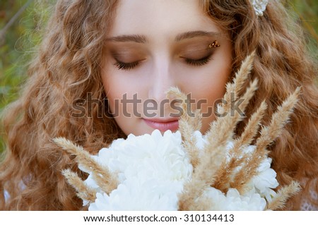 Woman with curly golden hair smiling with a bee on her pupils smelling flowers