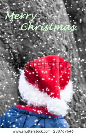 Merry christmas wish with little christmas elf in front of a huge tree in the snowy forest/Winter Christmas Imp with red pointed Hat and textual Christmas Wish