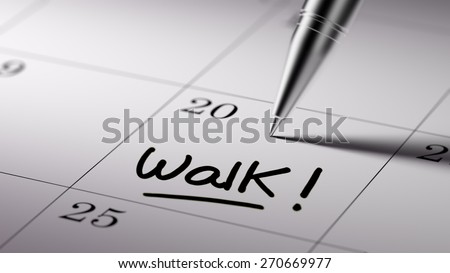Closeup of a personal agenda setting an important date written with pen. The words Walk written on a white notebook to remind you an important appointment.